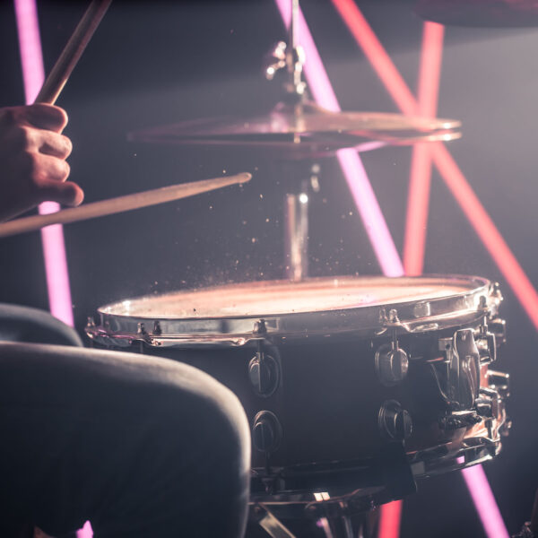 the man plays the drums, the game is on the working drum with sticks close-up. On the background of colored lights. Musical concept with a working drum.