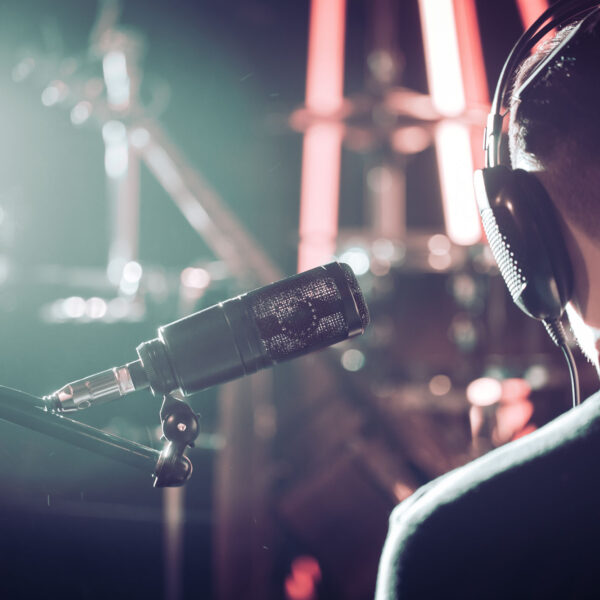 Person with headphones and Studio microphone close-up, in a recording Studio or concert hall, with a drum set on the background in out-of-focus mode. Beautiful blurred background of colored lanterns