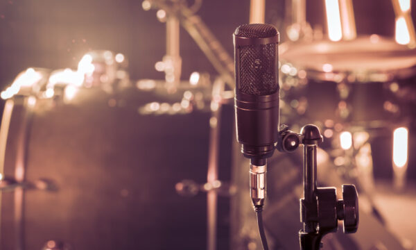 The microphone in a recording Studio or a concert hall close up of drum kit and an acoustic guitar in the background. Beautiful blurred background of colored lanterns. Musical concept in vintage style