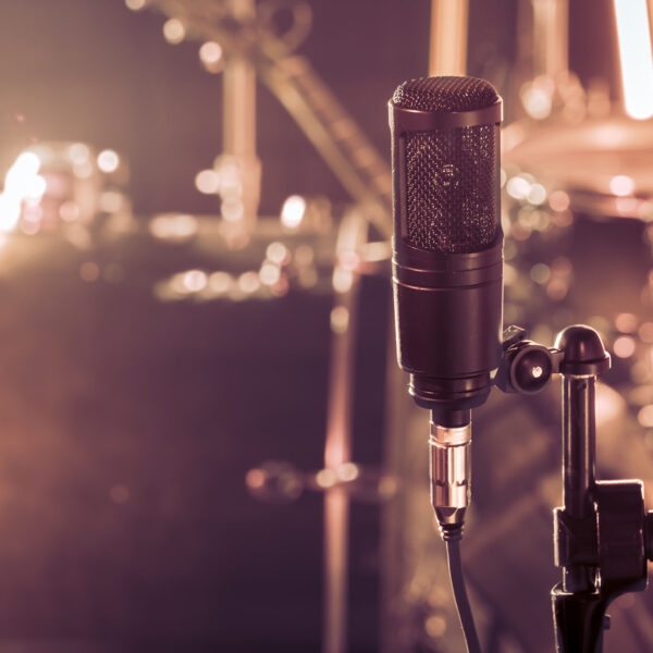 The microphone in a recording Studio or a concert hall close up of drum kit and an acoustic guitar in the background. Beautiful blurred background of colored lanterns. Musical concept in vintage style